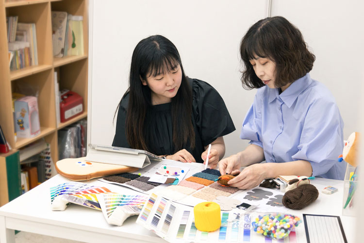 左：デザインチーム長のキム・ウンジさん、右：縫製室長：アン・ウンミさん。ロマネ社のオリジナルカラーを使ってキャラクターをデザイン。